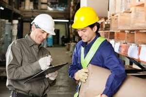 Young foreman looking at supervisor writing notes in warehouse